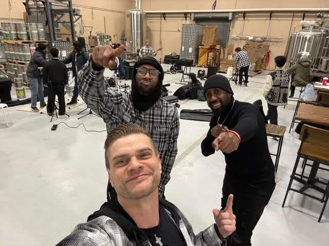 Three band members mugging for a selfie at a brewery video shoot